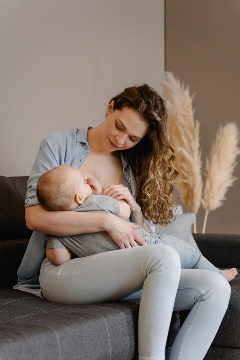 Mãe amamentando o bebê sentada no sofá de casa